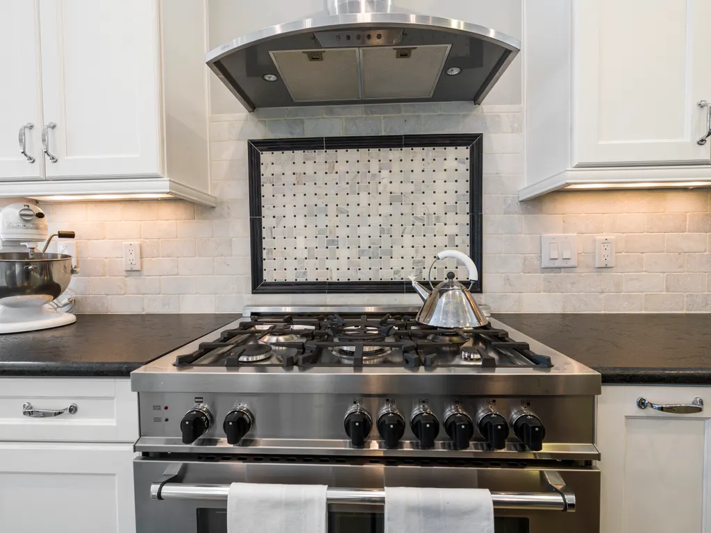 Illustrative stock photo of a stainless range hood above a stove, between white cabinets