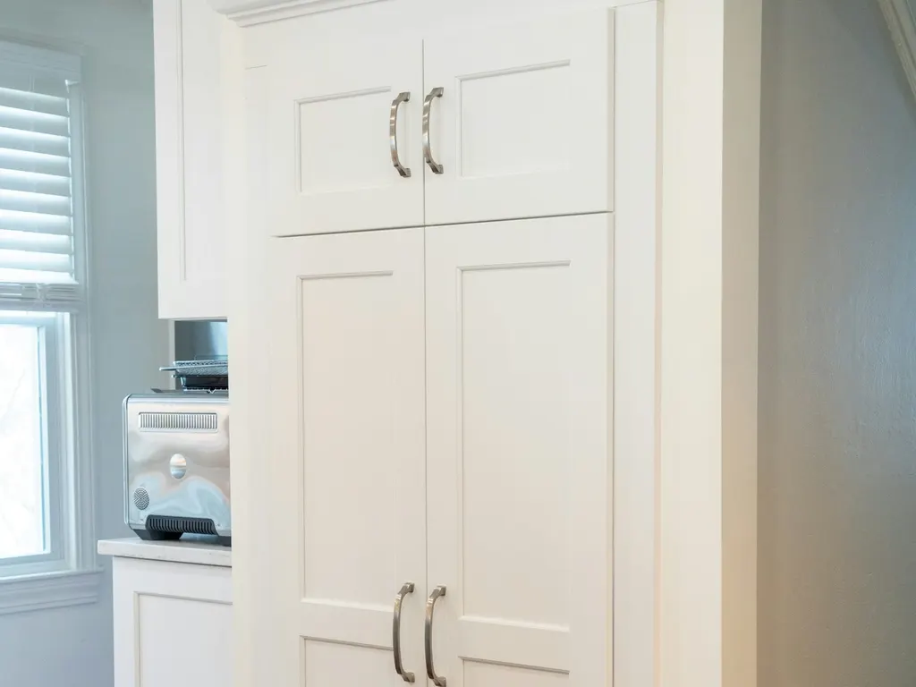 Illustrative photo of tall white cabinet-style door panels with brushed nickel handles, built into a kitchen wall